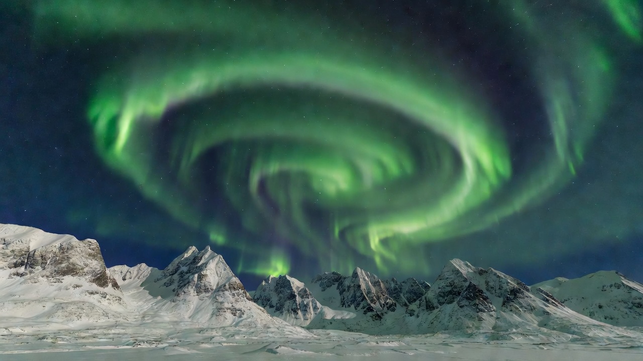 A sweeping curtain of aurora borealis curving over snow-covered peaks in northern Norway